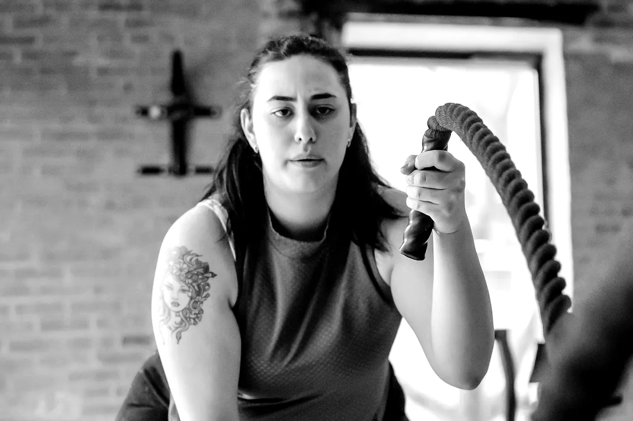 A member driving battle ropes against a brick wall, arms and shoulders working