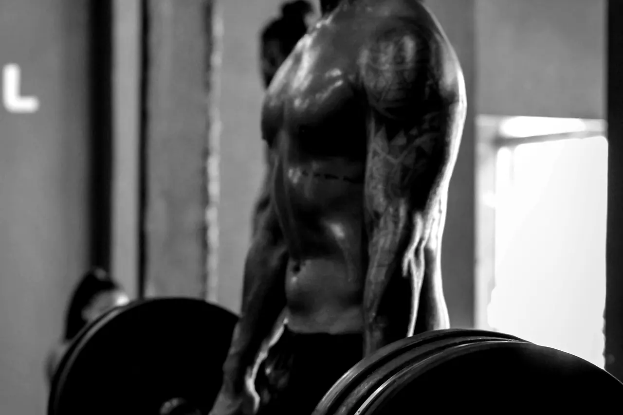 A lifter's back and shoulder under a bar, muscle definition and sweat picked out by hard side light