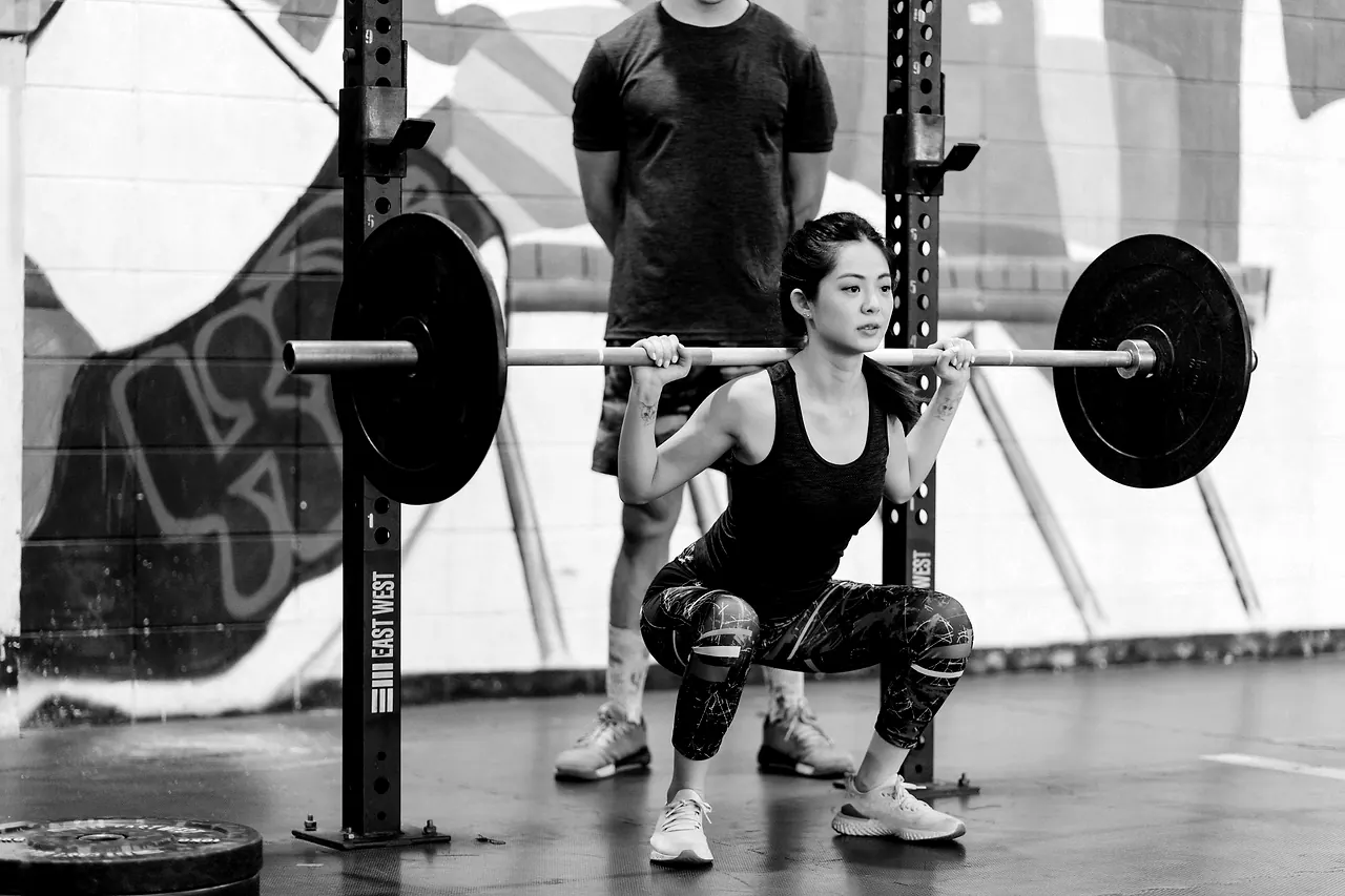 A coach standing behind a member learning the squat in the rack, watching the position