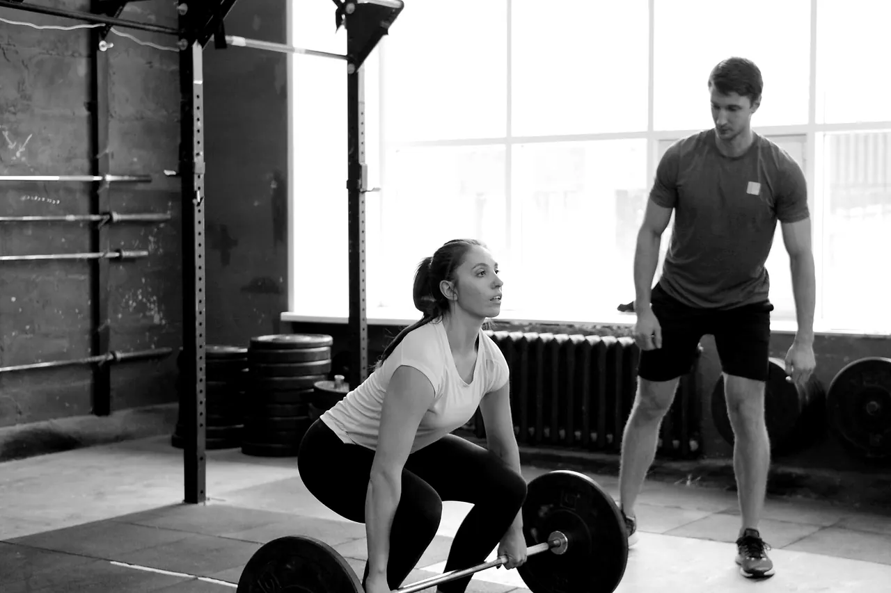 A member setting up a deadlift while a coach watches the position from the side