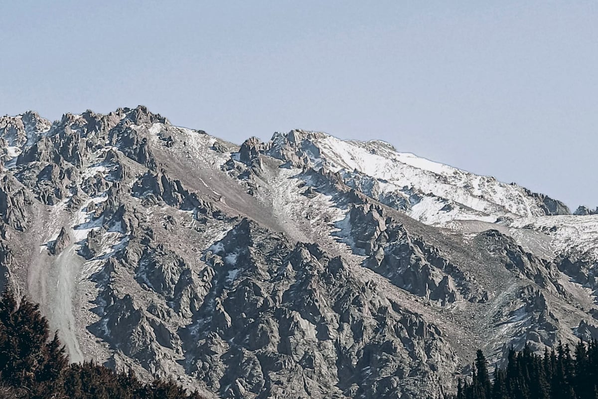 A hiker traversing an alpine ridge trail overlooking sweeping mountain peaks and green valleys