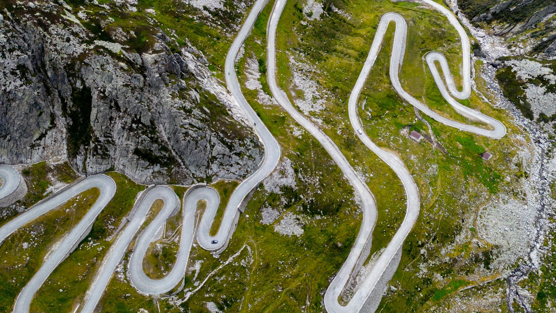 The pass road climbing toward the lodge above the valley, headlights tracing the switchbacks at dusk